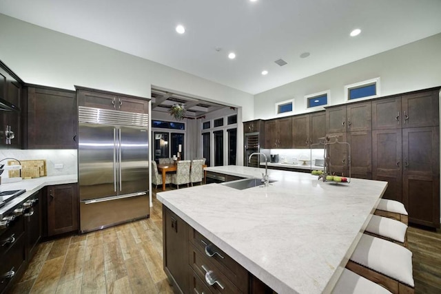 kitchen featuring sink, a kitchen breakfast bar, light hardwood / wood-style flooring, stainless steel built in fridge, and a center island with sink