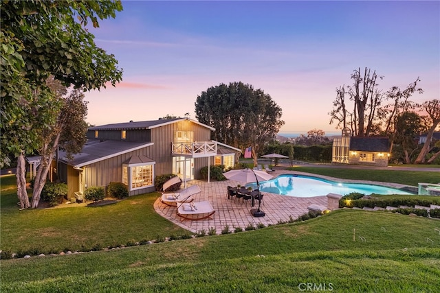 pool at dusk with a yard, a patio area, and an outbuilding