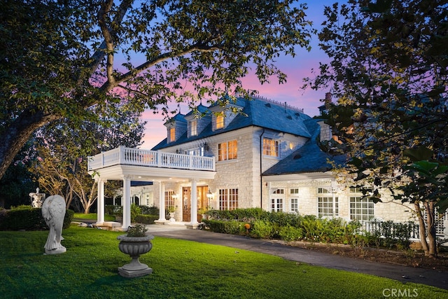 back house at dusk with a balcony and a yard