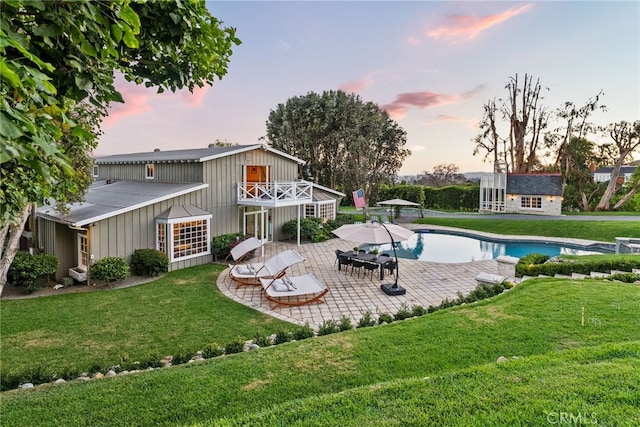 back house at dusk featuring a lawn and a patio