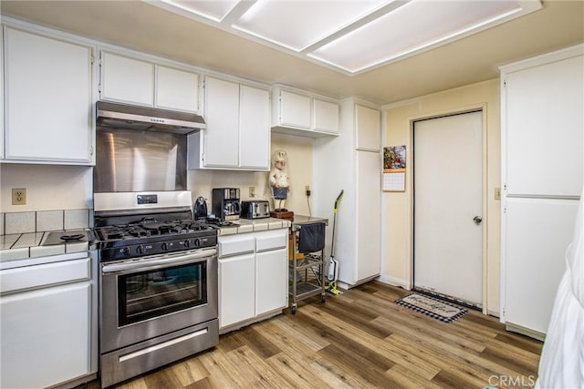 kitchen with white cabinets, gas range, exhaust hood, tile counters, and light hardwood / wood-style floors