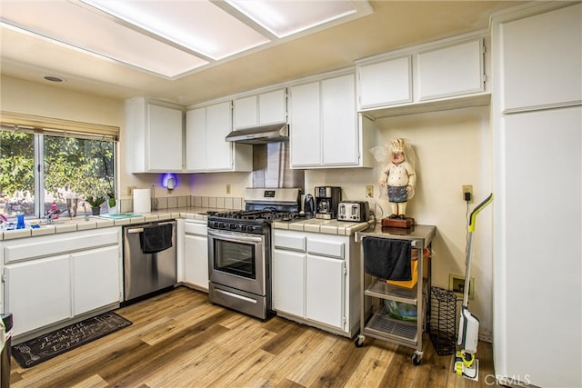 kitchen with white cabinetry, tile counters, appliances with stainless steel finishes, and light hardwood / wood-style floors