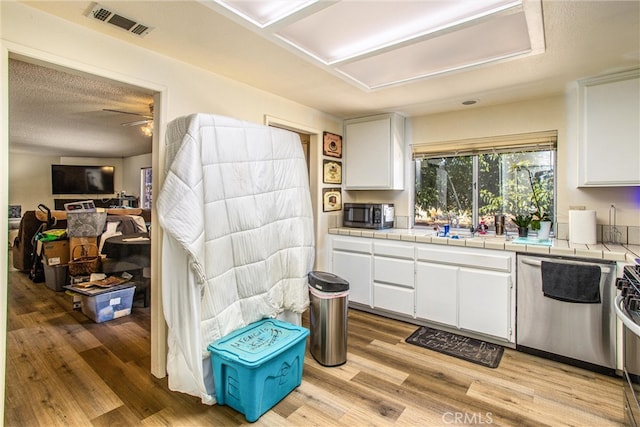 kitchen with white cabinets, light hardwood / wood-style floors, appliances with stainless steel finishes, and tile counters