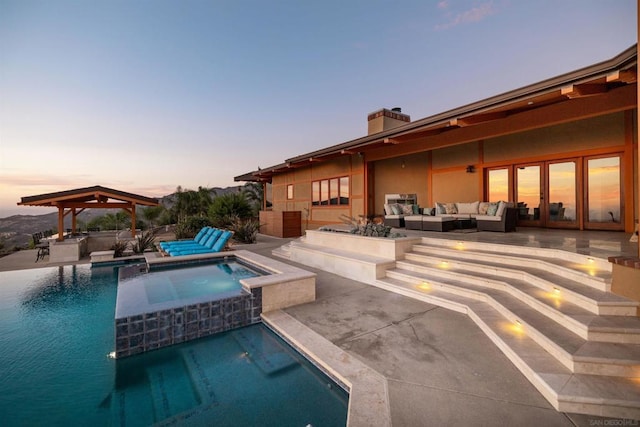 pool at dusk featuring an outdoor hangout area, an in ground hot tub, and a patio