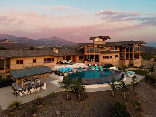 pool at dusk with a mountain view, exterior bar, and a patio