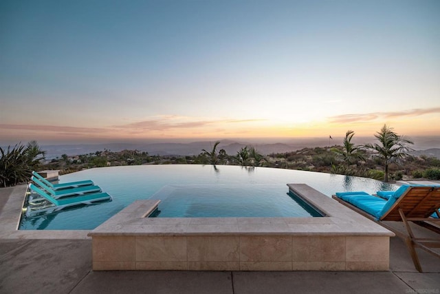 pool at dusk featuring an in ground hot tub