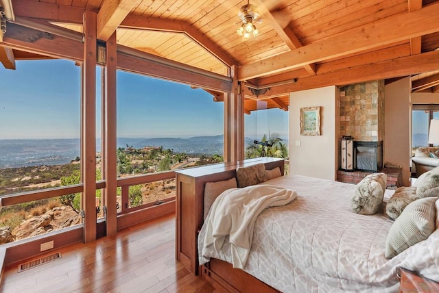 bedroom with a mountain view, wooden ceiling, lofted ceiling with beams, a large fireplace, and wood-type flooring