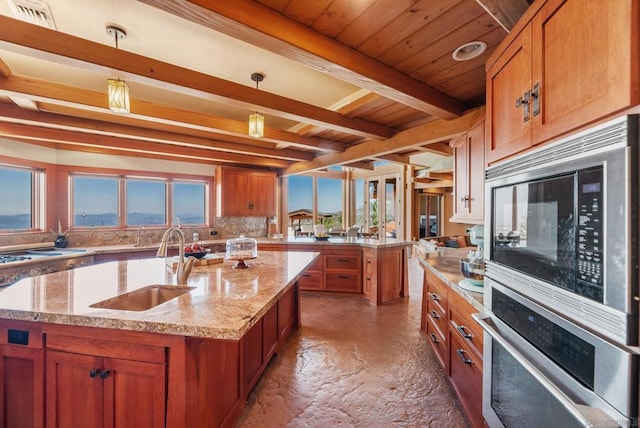 kitchen with tasteful backsplash, stainless steel appliances, sink, pendant lighting, and an island with sink