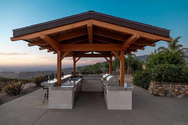 patio terrace at dusk featuring a gazebo, a mountain view, and area for grilling