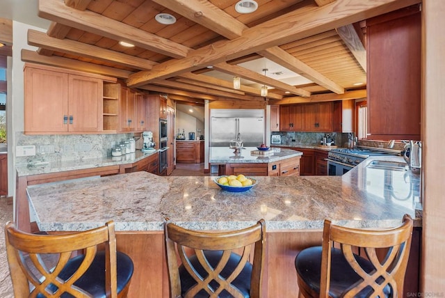 kitchen featuring kitchen peninsula, light stone countertops, beam ceiling, built in appliances, and a breakfast bar area