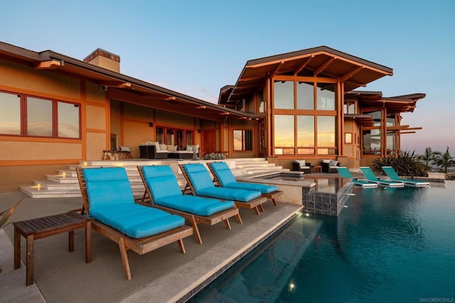 pool at dusk with outdoor lounge area, a patio area, and an in ground hot tub