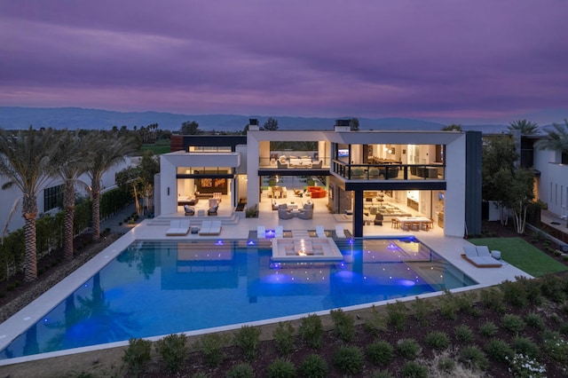 back house at dusk with a pool with hot tub, a balcony, and a patio area