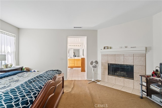 carpeted bedroom featuring ensuite bathroom and a tiled fireplace