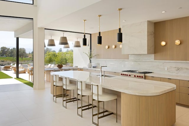 kitchen with sink, an island with sink, pendant lighting, and stainless steel gas stovetop