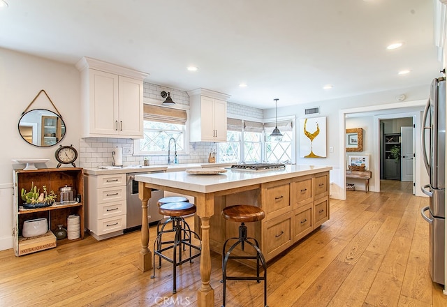 kitchen with a center island, white cabinets, hanging light fixtures, light hardwood / wood-style flooring, and stainless steel appliances