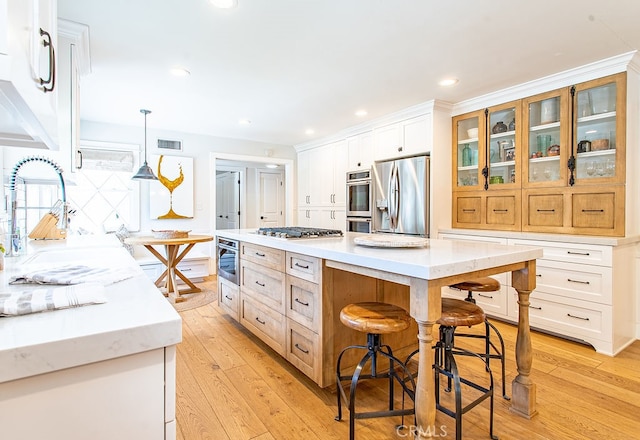 kitchen with stainless steel appliances, white cabinetry, light hardwood / wood-style floors, and a center island