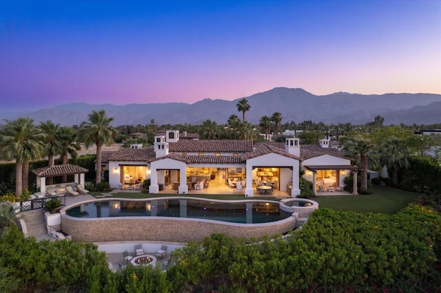 back house at dusk featuring a mountain view, a swimming pool with hot tub, a gazebo, and a patio