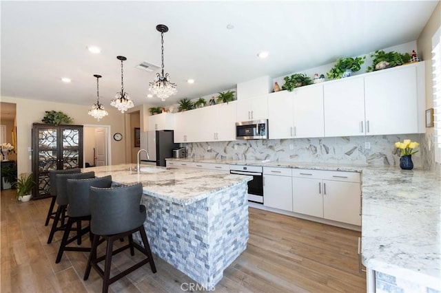 kitchen with tasteful backsplash, light hardwood / wood-style floors, a center island with sink, white cabinets, and appliances with stainless steel finishes