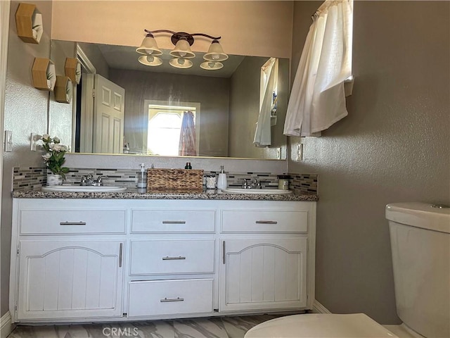 bathroom featuring double vanity, backsplash, a sink, and toilet