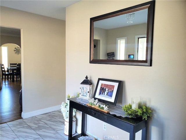 corridor featuring a wealth of natural light, arched walkways, marble finish floor, and baseboards