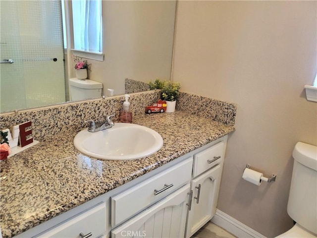 bathroom featuring a shower with shower door, baseboards, vanity, and toilet