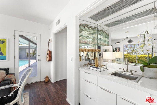 bar featuring dark wood-type flooring, sink, hanging light fixtures, and white cabinets