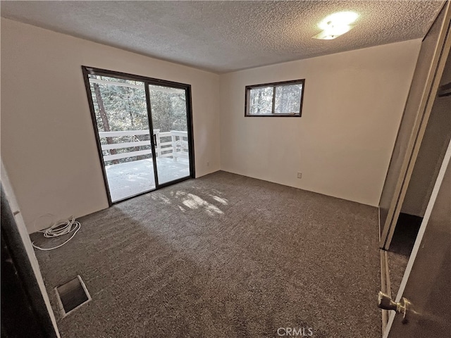 empty room featuring a wealth of natural light, dark colored carpet, and a textured ceiling