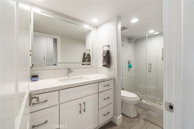 bathroom featuring wood-type flooring, toilet, vanity, and a shower with shower door