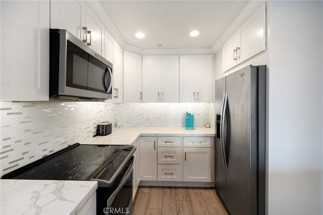 kitchen with appliances with stainless steel finishes, light stone counters, white cabinetry, and light hardwood / wood-style floors