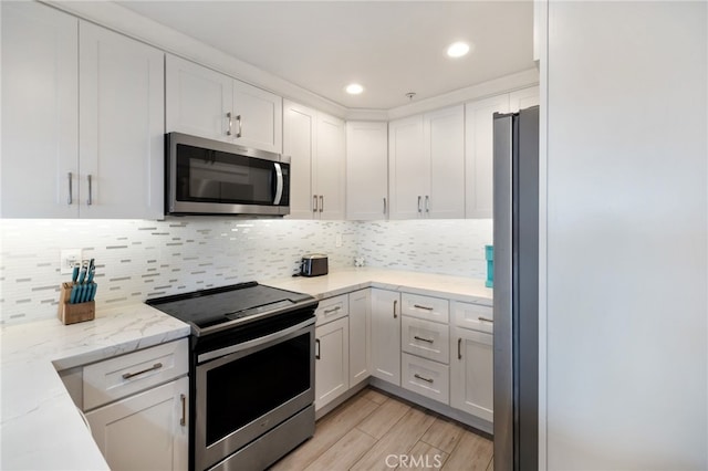 kitchen featuring light stone counters, white cabinets, light hardwood / wood-style floors, appliances with stainless steel finishes, and backsplash