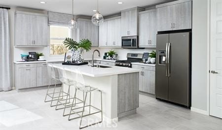 kitchen with a breakfast bar, stainless steel appliances, sink, decorative light fixtures, and an island with sink