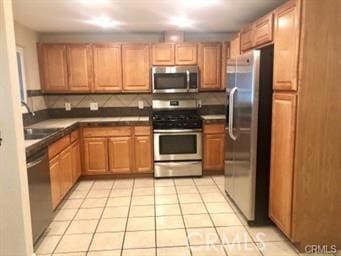 kitchen with appliances with stainless steel finishes, backsplash, sink, and light tile patterned floors