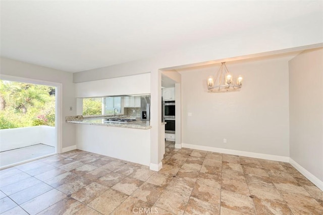 kitchen with tasteful backsplash, baseboards, appliances with stainless steel finishes, an inviting chandelier, and light countertops