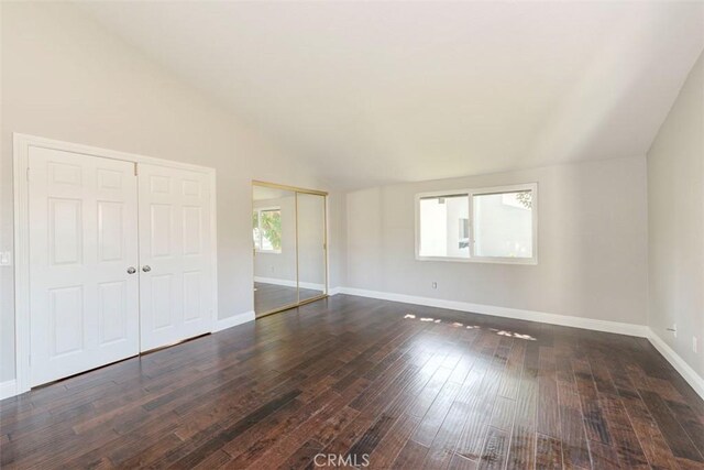 empty room featuring vaulted ceiling, dark wood-type flooring, and baseboards