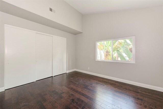 unfurnished bedroom with dark wood finished floors, a closet, visible vents, vaulted ceiling, and baseboards