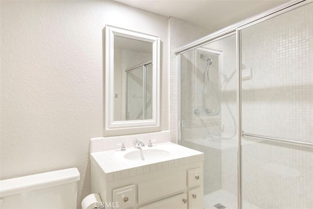 bathroom featuring a stall shower, a textured wall, vanity, and toilet