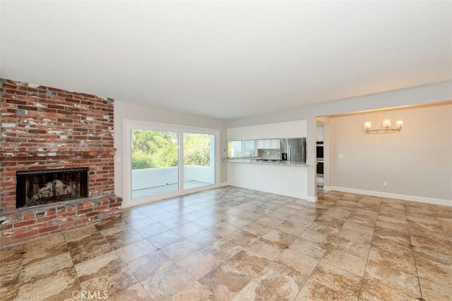 unfurnished living room featuring a brick fireplace and a notable chandelier