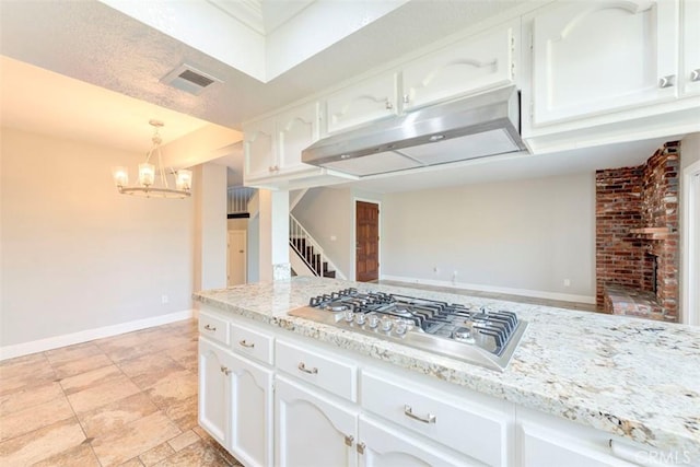 kitchen featuring visible vents, light stone counters, under cabinet range hood, stainless steel gas stovetop, and white cabinetry