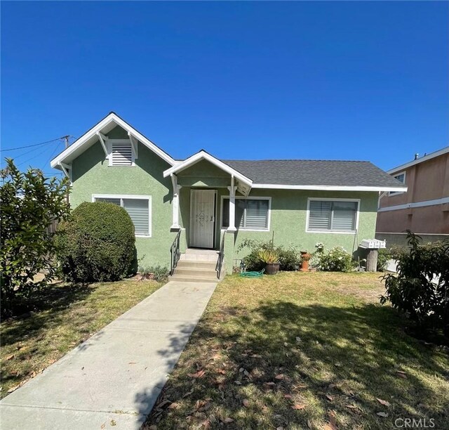 view of front of property featuring roof with shingles, a front yard, and stucco siding