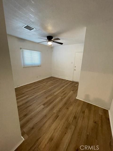 spare room with baseboards, a ceiling fan, wood finished floors, and visible vents