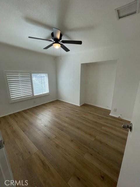 unfurnished room featuring wood finished floors, visible vents, a ceiling fan, and baseboards