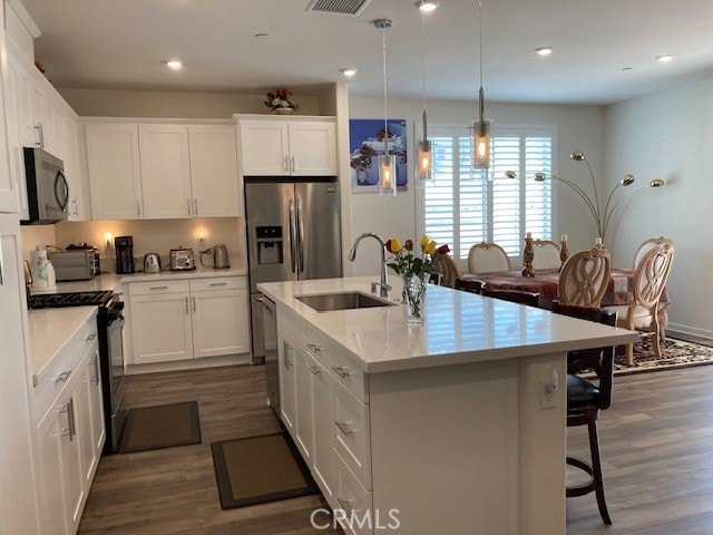 kitchen with sink, an island with sink, stainless steel appliances, and white cabinetry