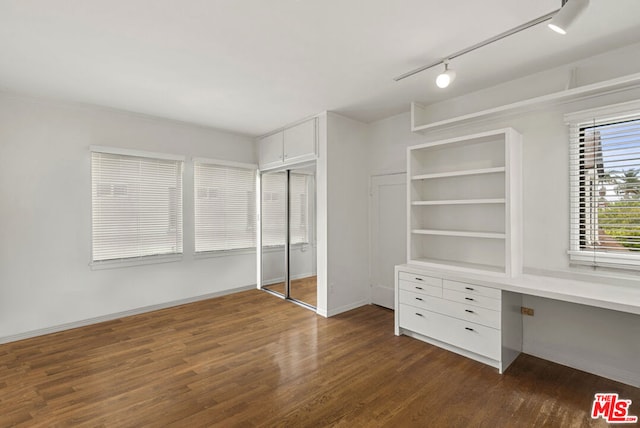 spacious closet featuring built in desk and dark wood-type flooring