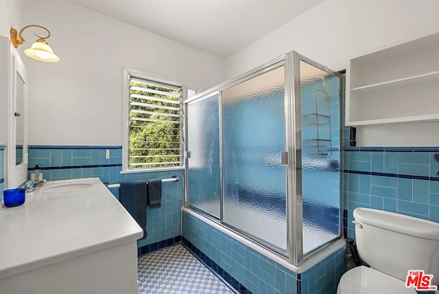 bathroom featuring tile walls, vanity, a shower with door, toilet, and tile patterned floors