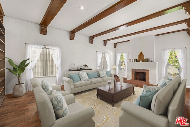 living room featuring a brick fireplace, beam ceiling, plenty of natural light, and dark wood-type flooring