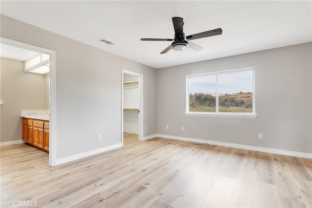 unfurnished bedroom with a spacious closet, connected bathroom, ceiling fan, and light hardwood / wood-style flooring