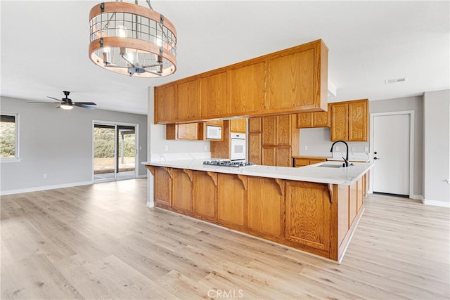 kitchen featuring light hardwood / wood-style floors, ceiling fan with notable chandelier, white oven, kitchen peninsula, and sink