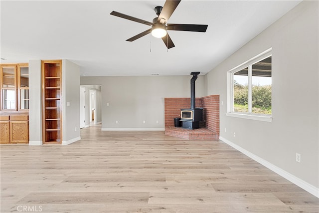 unfurnished living room featuring ceiling fan, a wood stove, and light hardwood / wood-style flooring