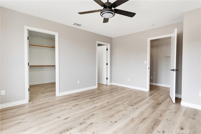 unfurnished bedroom with a spacious closet, a closet, ceiling fan, and light hardwood / wood-style flooring