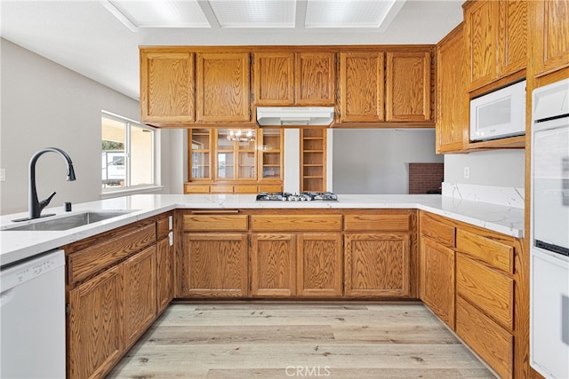 kitchen with light hardwood / wood-style floors, white appliances, sink, and kitchen peninsula